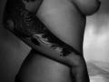 JeneKurz's bare side with a detailed black tattoo covering their arm, showing a fish with intricate patterns. JeneKurz's tits are visible, and their hand rests on their hip.