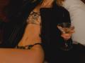 EolantaMarina with a slim, tan body, lace bra, and thong, black jacket, holding a martini glass, her ass and tits visible, lying on a bed.