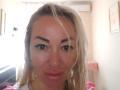 MysteryLaddy has wet blonde hair, thick black eyebrows, and shiny pink lips with a slight pout. She's wearing a white top, and her face is centered in the image.