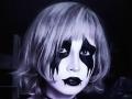 EmelyDilsaver with white face paint, black streaks, and black lipstick, has bleached blonde hair and a dark, moody expression in a grayscale photo.