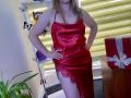 Aminas in a red satin dress with lace on the side, standing with hands on hips, showing her thighs and a tattoo on her right side.