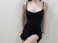 Ramilla wearing a black, ruched, spaghetti-strap dress with a slight hem lift, showing a bit of her thigh. She has a slim, pale, and slightly exposed chest.