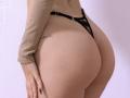 SugarrX's big ass in black lace thong, tan ribbed long-sleeve top, tattoo on right hip, light skin, hand with dark nails on left side.