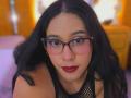 MarilynHills with long black hair, wearing glasses and red lipstick, looking forward with a serious expression, in a black fishnet top, showing her small tits.