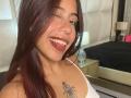 ScarletLuv with dark brown hair, nose ring, and lip ring, smiling with tongue out, showing white teeth. Has a spider tattoo on her right chest, wearing a white top.