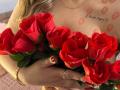 Niferttiti's tits, adorned with kiss marks, hold a bouquet of vibrant red roses. Her hand, with manicured nails and gold rings, cradles the flowers.