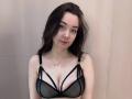 JuleeKasprzak has pale skin, dark wavy hair, and wears a black mesh bra with straps, revealing her tits. She's looking at the camera with a slight smile.