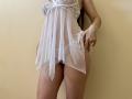Tisia wears a sheer white babydoll with lace top, exposing her small tits and pussy. She's pulling up the fabric, showing her bare, curvy thighs and hand.