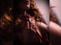 MalloryHearth with curly red hair, holding a red ribbon against her chest, showing her tits, in soft, dark lighting, focusing on her hand and upper body.