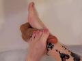 ElixirShanna's pink-painted toenails with glitter hold a flaccid, uncircumcised penis in a soapy white bathtub, her tattooed ankle visible.