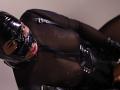 AntonellaVargas in black latex mask and sheer top, showing tits through mesh, with black leather straps, mouth open, tongue out, in a provocative, sexual, BDSM-themed photo.