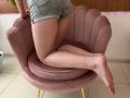Sanella's ass in tight gray shorts, kneeling on a pink, velvet chair with legs crossed, showing pale skin and bare feet. Pink fairy lights in the background.