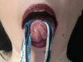 La bouche d'OrianaLaFrancaise est ouverte, et elle a des sous-vêtements bleus et blancs dans la bouche, sa langue est sortie, et elle porte du rouge à lèvres rouge foncé. Sa langue est visible et légèrement humide..