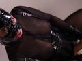 AntonellaVargas in black latex mask and sheer bodysuit, tongue out, looking up, with visible tits and nipple outlines, wearing leather straps, in a kinky, seductive pose.