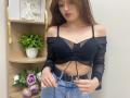 Rioria with long brown hair, black mesh off-shoulder top, showing her small tits, and blue jeans, adjusting her belt. She's looking down, with hoop earrings.