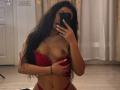 Emma Noor, avec ses longs cheveux noirs, tenant un téléphone devant son visage, portant un soutien-gorge en dentelle rouge, relevé pour exposer ses seins, et une culotte rouge, recouvrant son sein droit..