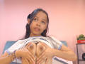 AuroraBellinii with dark hair, wearing a lifted shirt, holding her small tits with her hands, pink wall background, bracelet on left wrist, soft expression, pinkish skin.
