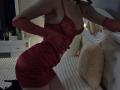Rozalin in a red, sheer, lace lingerie dress with long gloves, showing off her tits and ass, leaning forward on a bed with a fluffy pillow.