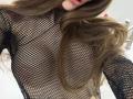 SensualMila in a black fishnet top, her brown hair covering her tits, nipples visible through the mesh. Her lips are slightly parted. Bathroom sink in the background.