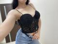 OliviaGranda with black lace bralette, showing her tits, in blue jeans, hand in pocket, long dark hair, white wall, brown door, and a silver necklace in a selfie.