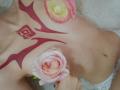 AmeliaMaiv's topless torso with red tribal tattoos, pink and white roses covering her tits, and lace panties. Her skin is light, and she's lying on a fluffy white surface.