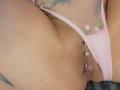 FrenchShanna's pink mesh and floral underwear, exposing her pierced pussy with a silver ring. Her tan skin shows a small tattoo near her left hip.
