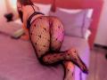 LaraHarvey on a bed, wearing black fishnet tights with diamond patterns, blue bra, and a visible pink pussy, on all fours, with her ass raised.