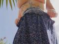 FrenchieLilieFleur with tattoos on her side and belly, pulling down a dark floral skirt, showing a bit of her belly and tattoos, taken from a low angle.