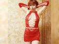 LaylaHottyX with red mesh dress, large cutouts, and arms raised, showing pale skin and red hair, wearing red earrings, standing in a room with gold-patterned wallpaper.
