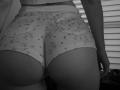 SugarrX's butt in tight, floral-patterned shorts, showing a round, bare buttcheek, with her hand slightly visible on the right. Black and white, from behind.