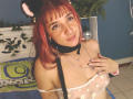 SamanthaaMiller with red hair, cat ears, black collar, and leash, wearing sheer floral top, exposing small tits, smiling, hand on chest, nose ring, in cozy room.