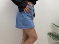 Tilliana's blue denim skirt, buttoned up, with black long-sleeve top, pink nails, hand on hip, and tan legs, showing a small part of her pink-nipled belly.
