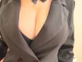 Il blazer nero di EmmaNoa è aperto, rivelando il suo seno abbondante. La sua pelle chiara contrasta con il tessuto scuro, e una cravatta nera è visibile nella parte superiore..