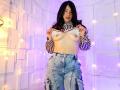 NinaHarpper with long black hair, striped top lifted to expose her bare tits, wearing high-waisted, ripped blue jeans, standing in a softly lit room with fairy lights.