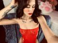 HarleyRoods with red lace bodysuit, showing her tits and ass, dark wavy hair, red lipstick, tattoos, and blue blanket in a bedroom selfie.