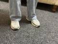 Dalaila's feet in dirty beige sneakers, standing on grey carpet. She's wearing light blue, slightly baggy jeans. Sneakers are slightly worn, showing some dirt and wear.