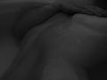 NievesMegee's wet, dark-skinned back with a hand resting above her ass in a black-and-white, close-up, dark-photograph-style image. Her smooth, glistening skin is visible.