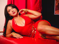 LilyConorr with big tits, wearing a red dress, gold bracelets, and red lipstick, lying on a red leather couch, looking sexy, her ass partially exposed, dark hair, red eyes.