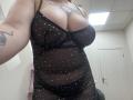 DiLaria, avec de grandes seins ronds, porte une robe noire transparente à pois, qui révèle sa poitrine et ses tatouages, et prend un selfie dans une pièce avec une porte blanche..