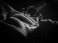 NyraVanel's tits are exposed, with smoke swirling around her chest and neck. She's lying down, dark background, black-and-white, sensual, and partially shadowed.