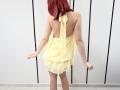 JuliannaMoor with red hair, back to camera, wearing a yellow halter dress, showing her bare ass and back, standing with arms slightly out, in a white room.