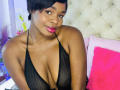 VenusWilly with short black hair, wearing a black mesh halter top, exposing her big, shiny tits, and pink lipstick, smiling slightly, in a bedroom with a pink pillow.