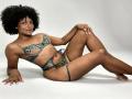RoldanStefy with dark curly hair, tan skin, and small to medium tits, wearing green lace lingerie, lying on white floor, legs bent, smiling, right arm supporting upper body.