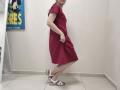 JoannaSia's red dress, white wedge sandals, and hand in pocket, standing with a slight sideways bend, exposing her ass and small tits. She's in a plain room.