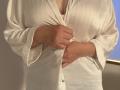 Elliance's hands are buttoning up a white, silky blouse that reveals her sizable, rounded tits. Her skin is light, and the blouse is slightly open at the bottom.