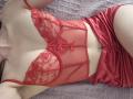 Rozalin in red lace lingerie with heart patterns and a small bow, wearing matching satin shorts, lying on a purple textured surface, showing her tits and slim waist.